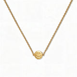 A Skōsh Kids Smiley Face Necklace by Skōsh Jewelry, featuring a small round smiley face charm set sideways on a fine gold chain, displayed against a white background.