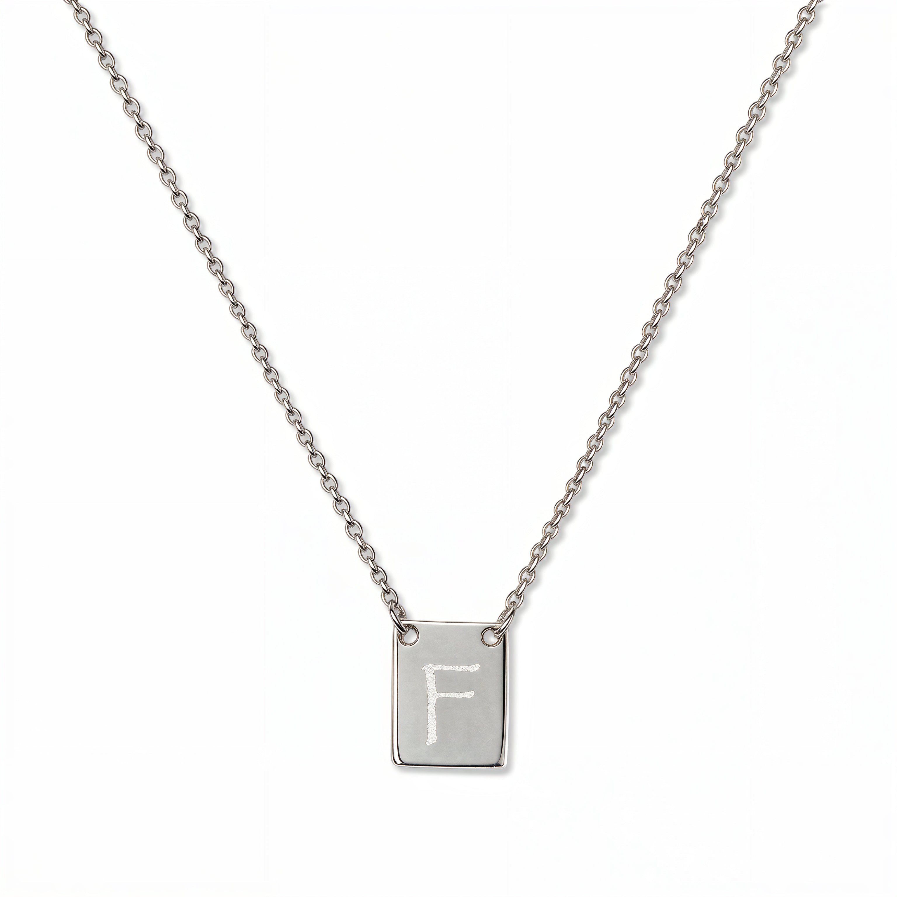 An Engraved Initial Necklace Letter F by Skōsh Jewelry, featuring a small rectangular tag engraved with the letter F on a fine sterling silver chain, displayed against a white background.