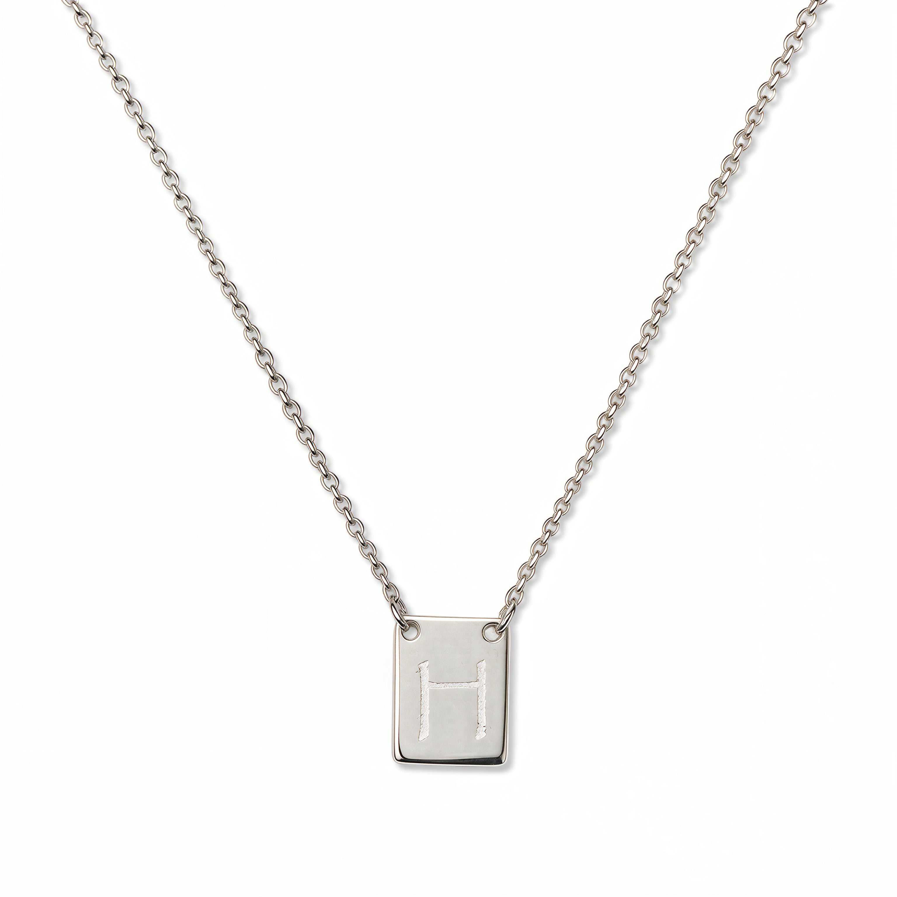 An Engraved Initial Necklace Letter H by Skōsh Jewelry, featuring a small rectangular tag engraved with the letter H on a fine sterling silver chain, displayed against a white background.