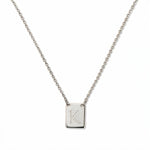 An Engraved Initial Necklace Letter K by Skōsh Jewelry, featuring a small rectangular tag engraved with the letter K on a fine sterling silver chain, displayed against a white background.