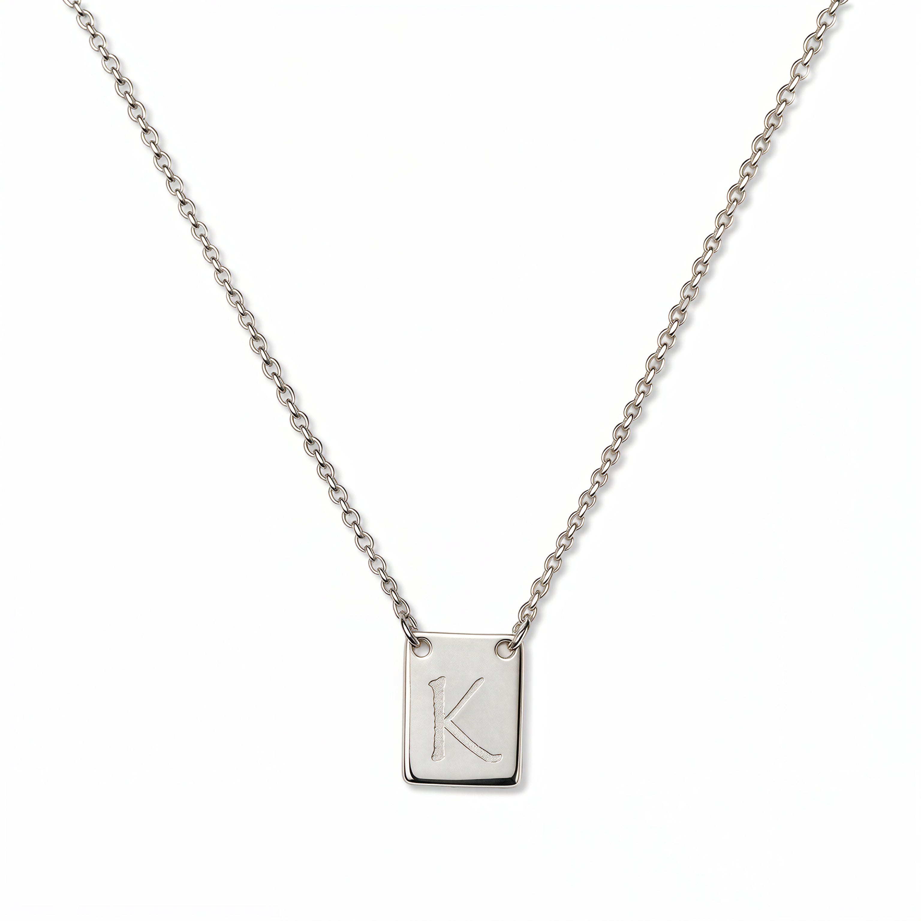 An Engraved Initial Necklace Letter K by Skōsh Jewelry, featuring a small rectangular tag engraved with the letter K on a fine sterling silver chain, displayed against a white background.