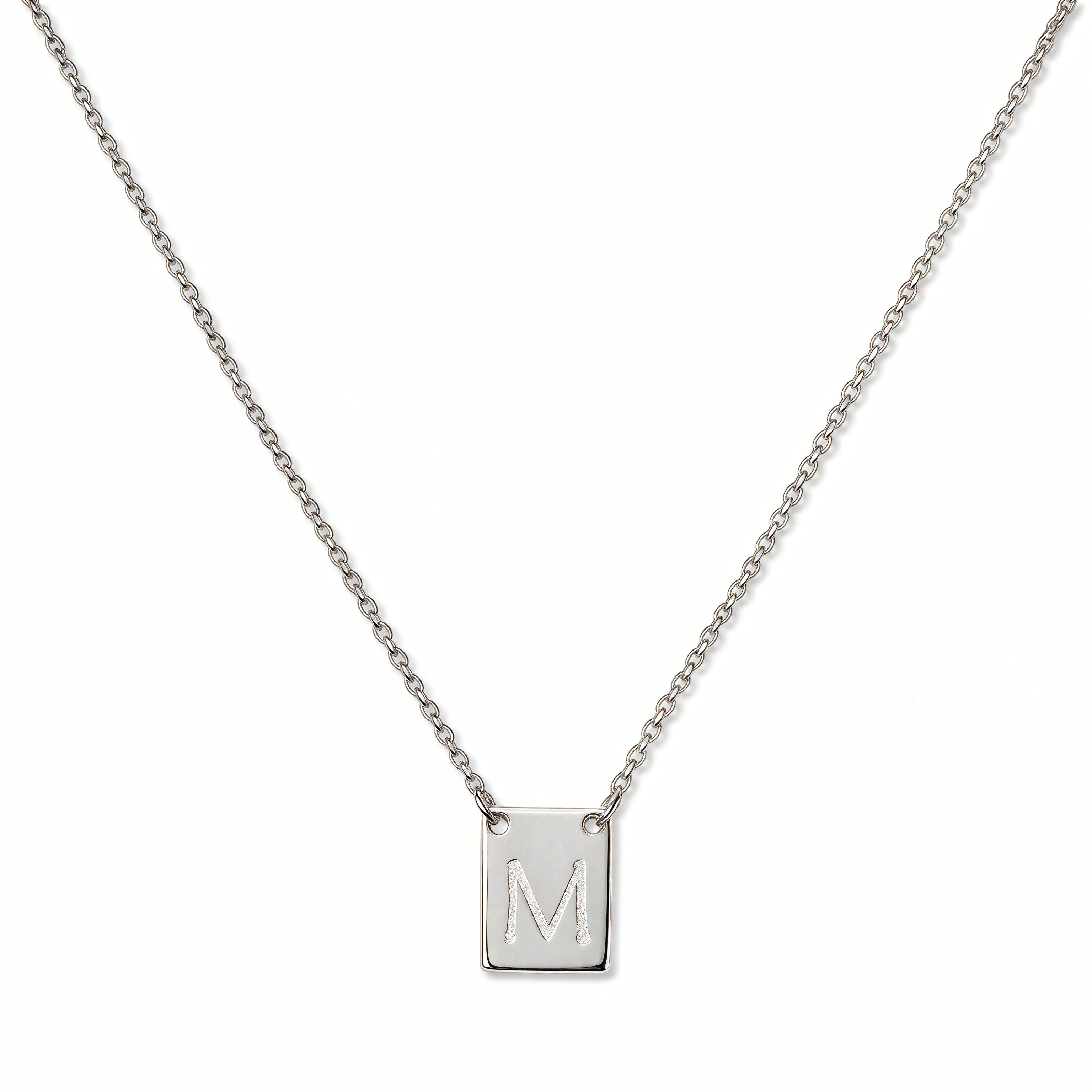 An Engraved Initial Necklace Letter M by Skōsh Jewelry, featuring a small rectangular tag engraved with the letter M on a fine sterling silver chain, displayed against a white background.
