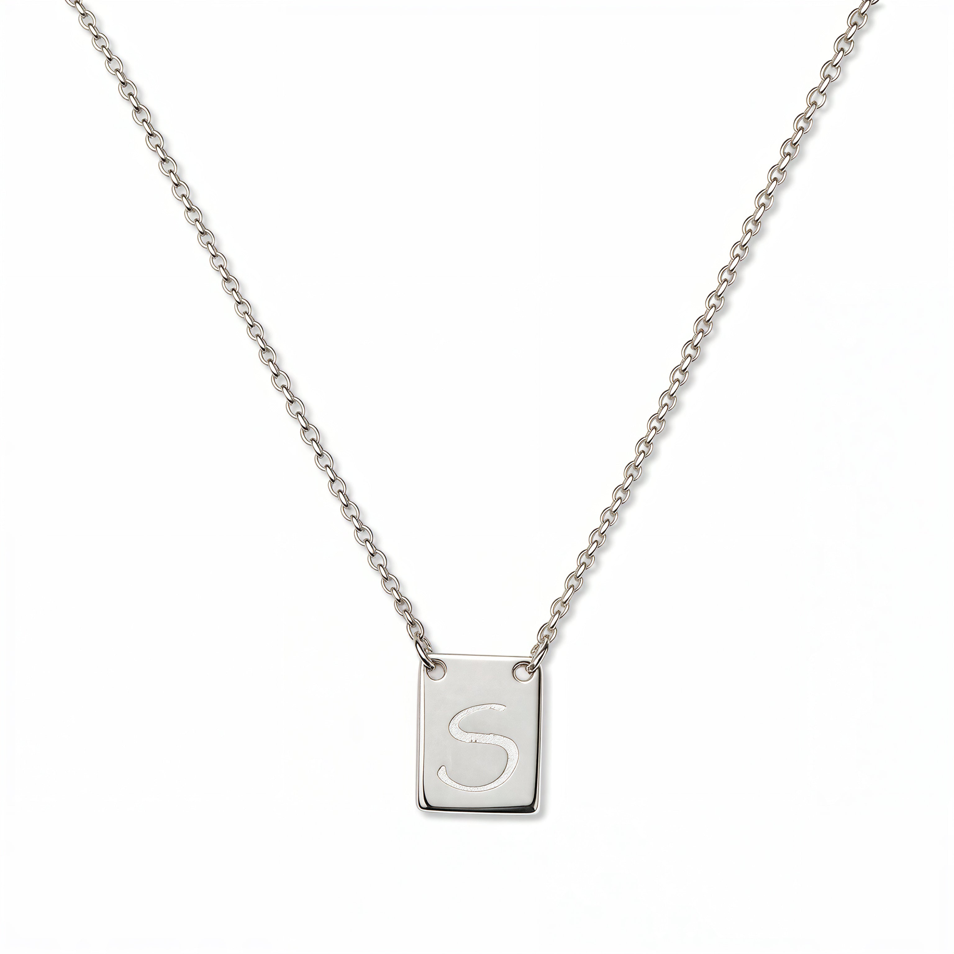 An Engraved Initial Necklace Letter S by Skōsh Jewelry, featuring a small rectangular tag engraved with the letter S on a fine sterling silver chain, displayed against a white background.