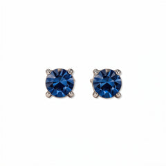 A pair of September Birthstone Round Sapphire Cubic Zirconia Stud Earrings by Skōsh Jewelry, featuring faceted deep blue round stones in a four-prong sterling silver setting, displayed against a white background.