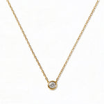 A Stillness Bezel Set White Cubic Zirconia Necklace by Skōsh Jewelry, featuring a single round clear stone in a smooth bezel setting on a fine gold chain, displayed against a white background.