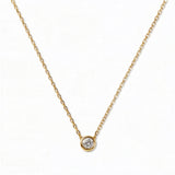 A Stillness Bezel Set White Cubic Zirconia Necklace by Skōsh Jewelry, featuring a single round clear stone in a smooth bezel setting on a fine gold chain, displayed against a white background.