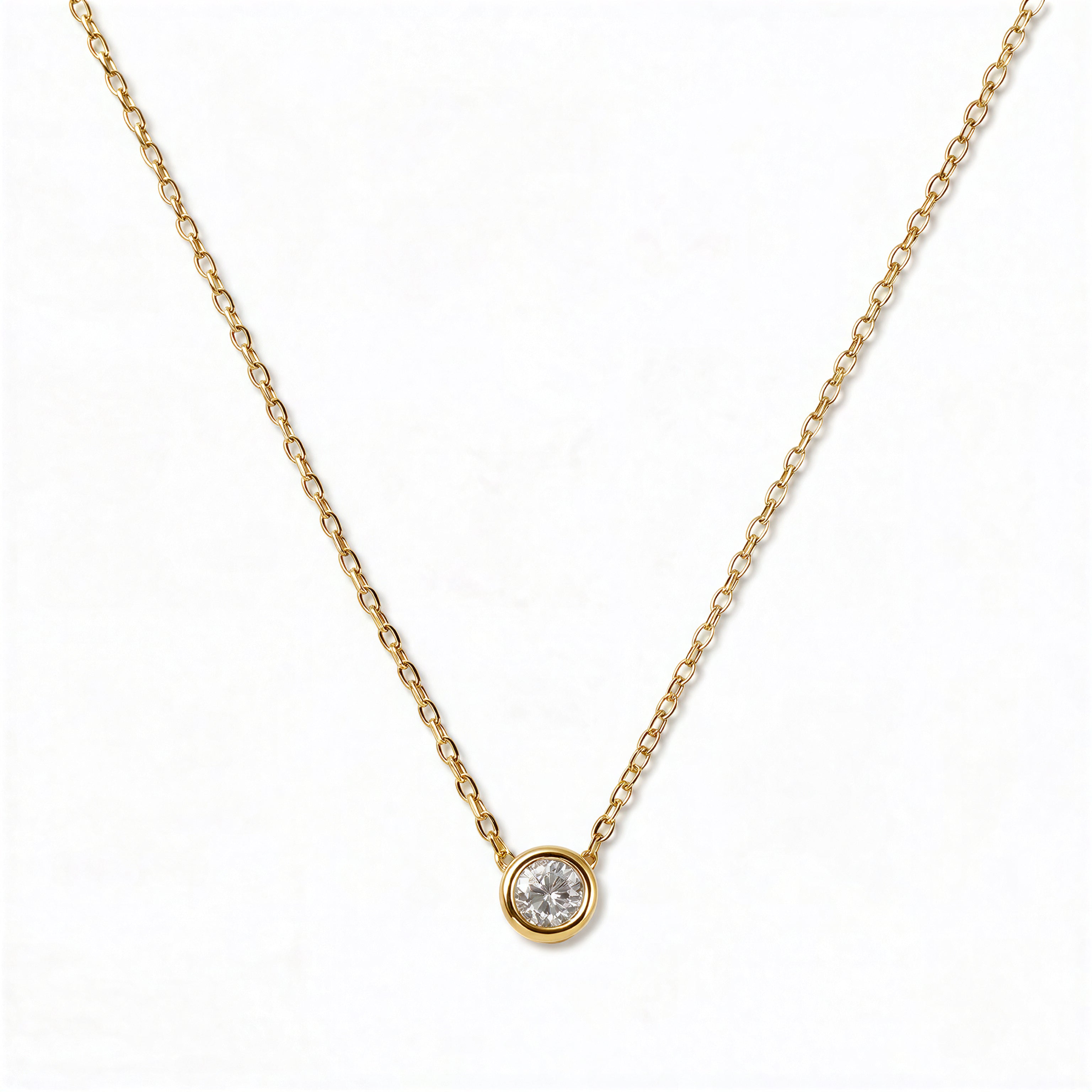 A Stillness Bezel Set White Cubic Zirconia Necklace by Skōsh Jewelry, featuring a single round clear stone in a smooth bezel setting on a fine gold chain, displayed against a white background.
