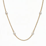 A Nine Station Freshwater Pearl Necklace by Skōsh Jewelry, featuring small white freshwater pearls spaced evenly along a fine gold station chain, displayed against a white background.