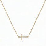 A Devoted White Cubic Zirconia Sideways Cross Necklace by Skōsh Jewelry, featuring a sideways cross lined with small clear pavé stones on a fine gold chain, displayed against a white background.