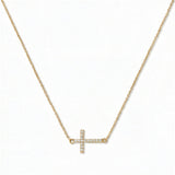A Devoted White Cubic Zirconia Sideways Cross Necklace by Skōsh Jewelry, featuring a sideways cross lined with small clear pavé stones on a fine gold chain, displayed against a white background.