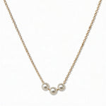 A Timeless Trio Freshwater Pearl Necklace by Skōsh Jewelry, featuring three white freshwater pearls in a row along a fine gold chain, displayed against a white background.