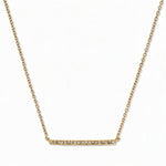 A Luminary White Cubic Zirconia Bar Necklace by Skōsh Jewelry, featuring a long slim bar lined with small clear stones on a fine gold chain, displayed against a white background.
