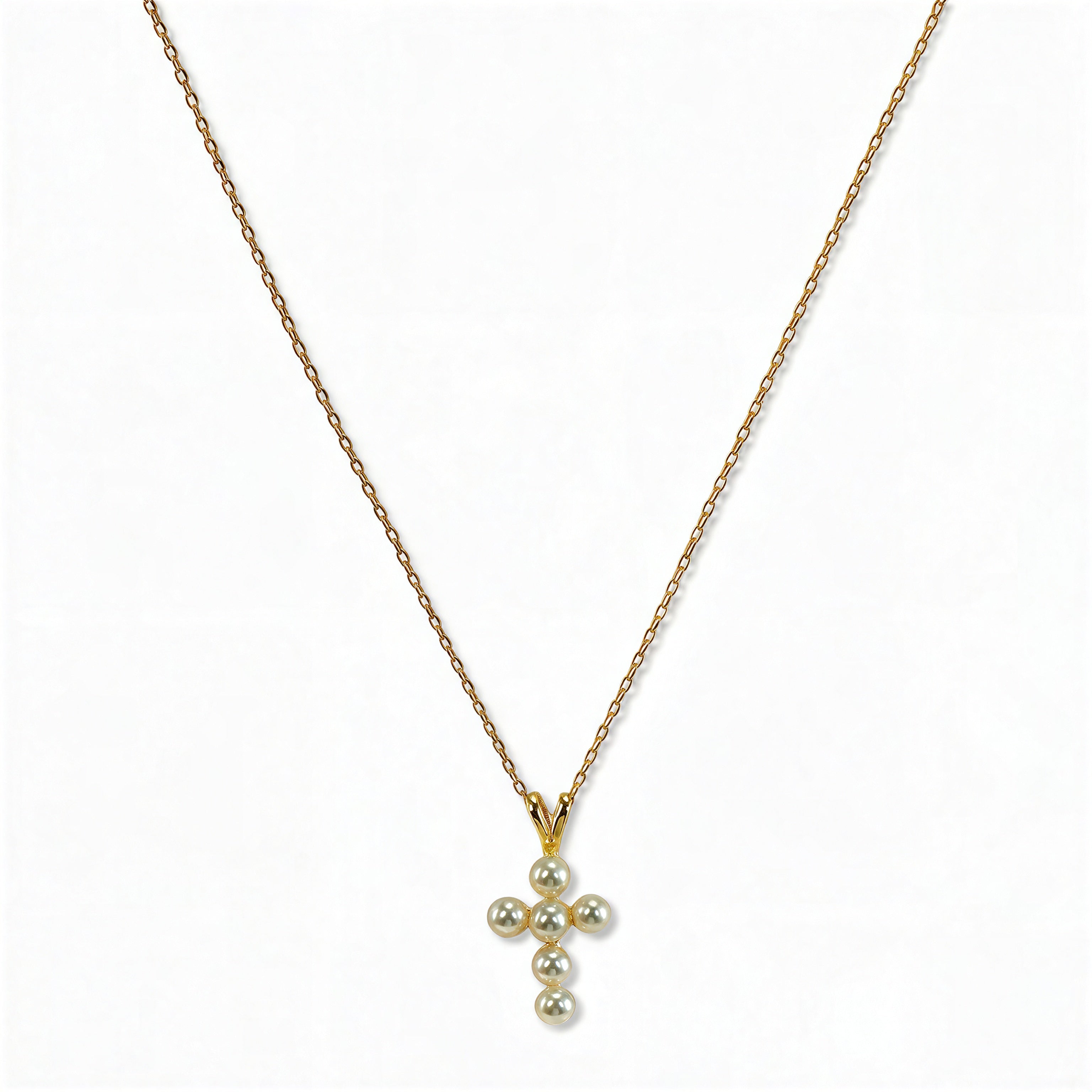 A Blessing Freshwater Pearl Mini Cross Necklace by Skōsh Jewelry, featuring a small cross pendant made of tiny white pearl beads hanging from a fine gold chain, displayed against a white background.