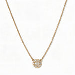 A Luna Glow Pavé Disc White Cubic Zirconia Necklace by Skōsh Jewelry, featuring a round disc covered in small clear pavé stones on a fine gold chain, displayed against a white background.