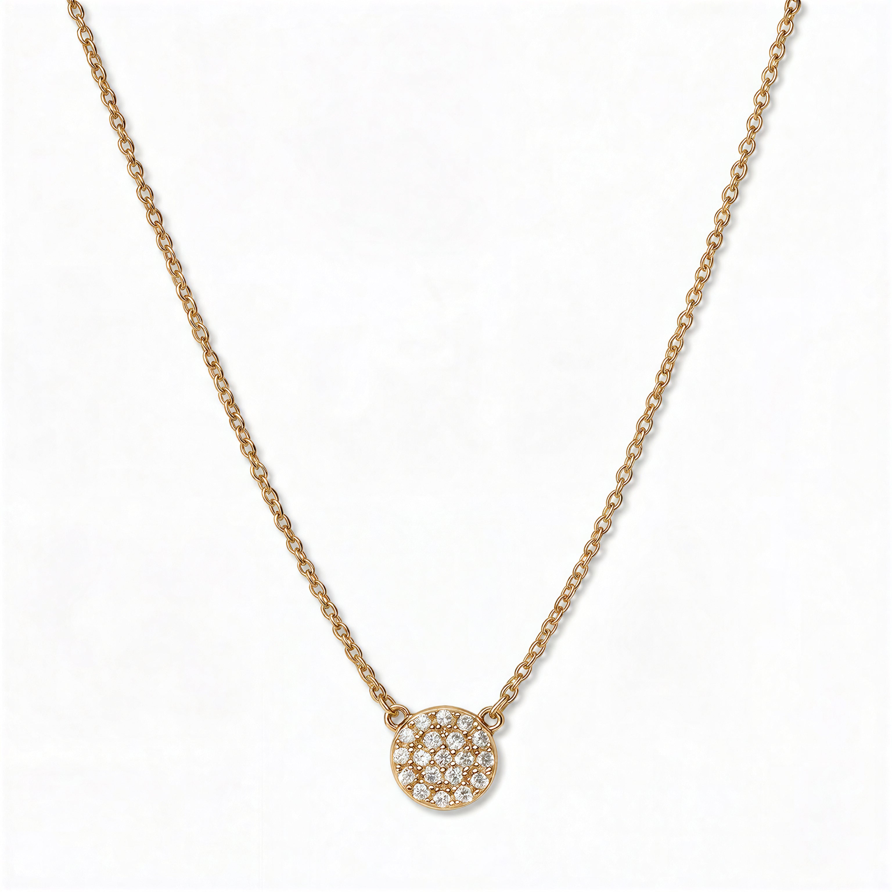 A Luna Glow Pavé Disc White Cubic Zirconia Necklace by Skōsh Jewelry, featuring a round disc covered in small clear pavé stones on a fine gold chain, displayed against a white background.