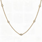 A Starlight Strand Bezel Station White Cubic Zirconia Necklace by Skōsh Jewelry, featuring small round clear stones in bezel settings spaced along a fine gold chain, displayed against a white background.