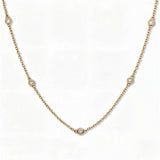 A Starlight Strand Bezel Station White Cubic Zirconia Necklace by Skōsh Jewelry, featuring small round clear stones in bezel settings spaced along a fine gold chain, displayed against a white background.