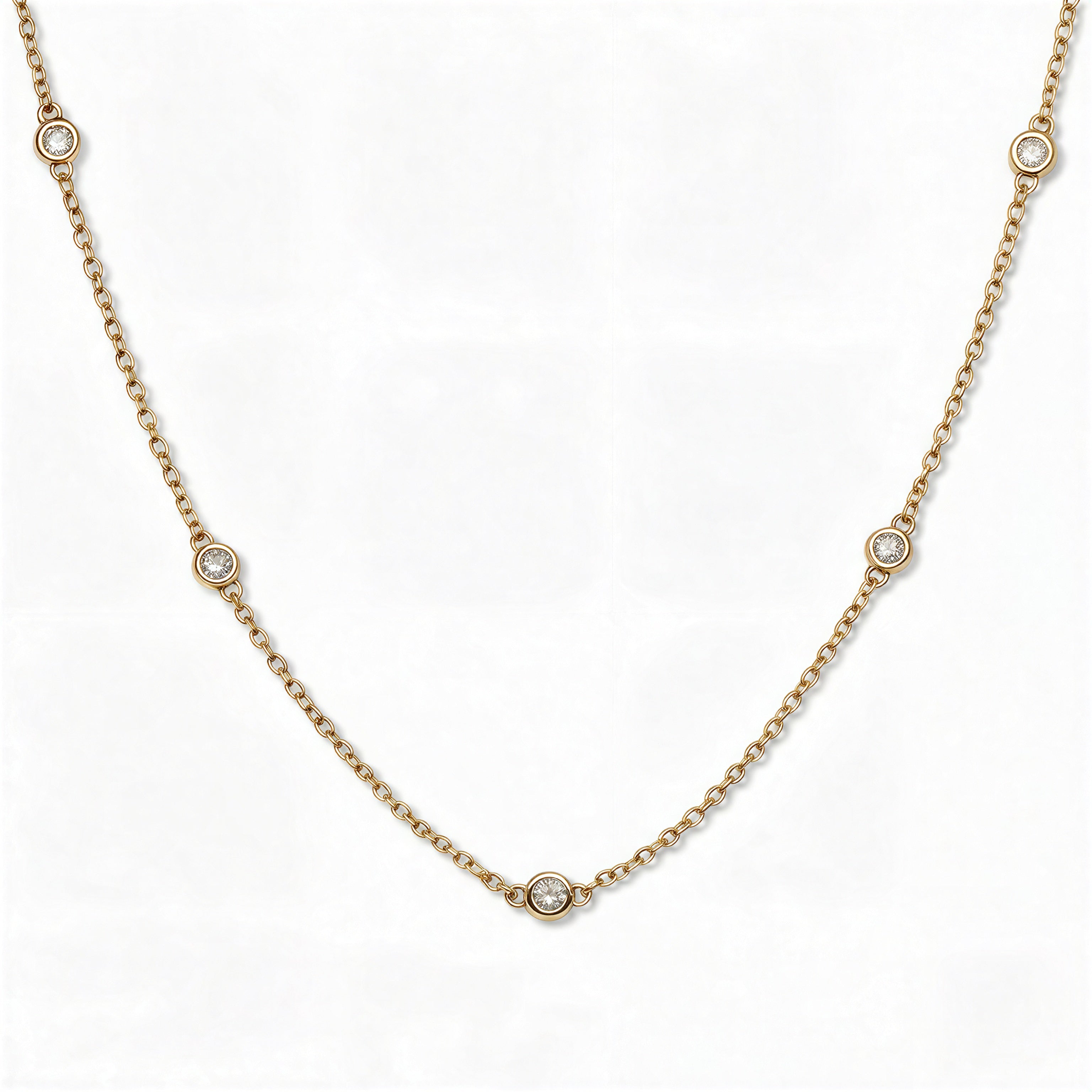 A Starlight Strand Bezel Station White Cubic Zirconia Necklace by Skōsh Jewelry, featuring small round clear stones in bezel settings spaced along a fine gold chain, displayed against a white background.
