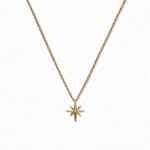 A North Star White Cubic Zirconia Accent Pendant Necklace by Skōsh Jewelry, featuring an eight-point star pendant with a small clear stone at its center on a fine gold chain, displayed against a white background.