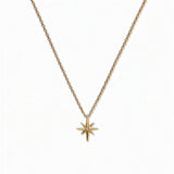 A North Star White Cubic Zirconia Accent Pendant Necklace by Skōsh Jewelry, featuring an eight-point star pendant with a small clear stone at its center on a fine gold chain, displayed against a white background.