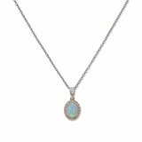 An Ethereal Opal with White Cubic Zirconia Halo Pendant Necklace by Skōsh Jewelry, featuring an oval iridescent opal framed by a halo of small clear stones on a fine sterling silver chain, displayed against a white background.