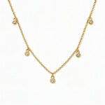 A Halo Bezel Set White Cubic Zirconia Drop Station Necklace by Skōsh Jewelry, featuring small bezel-set clear stones dangling at intervals along a fine gold chain, displayed against a white background.