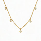 A Halo Bezel Set White Cubic Zirconia Drop Station Necklace by Skōsh Jewelry, featuring small bezel-set clear stones dangling at intervals along a fine gold chain, displayed against a white background.