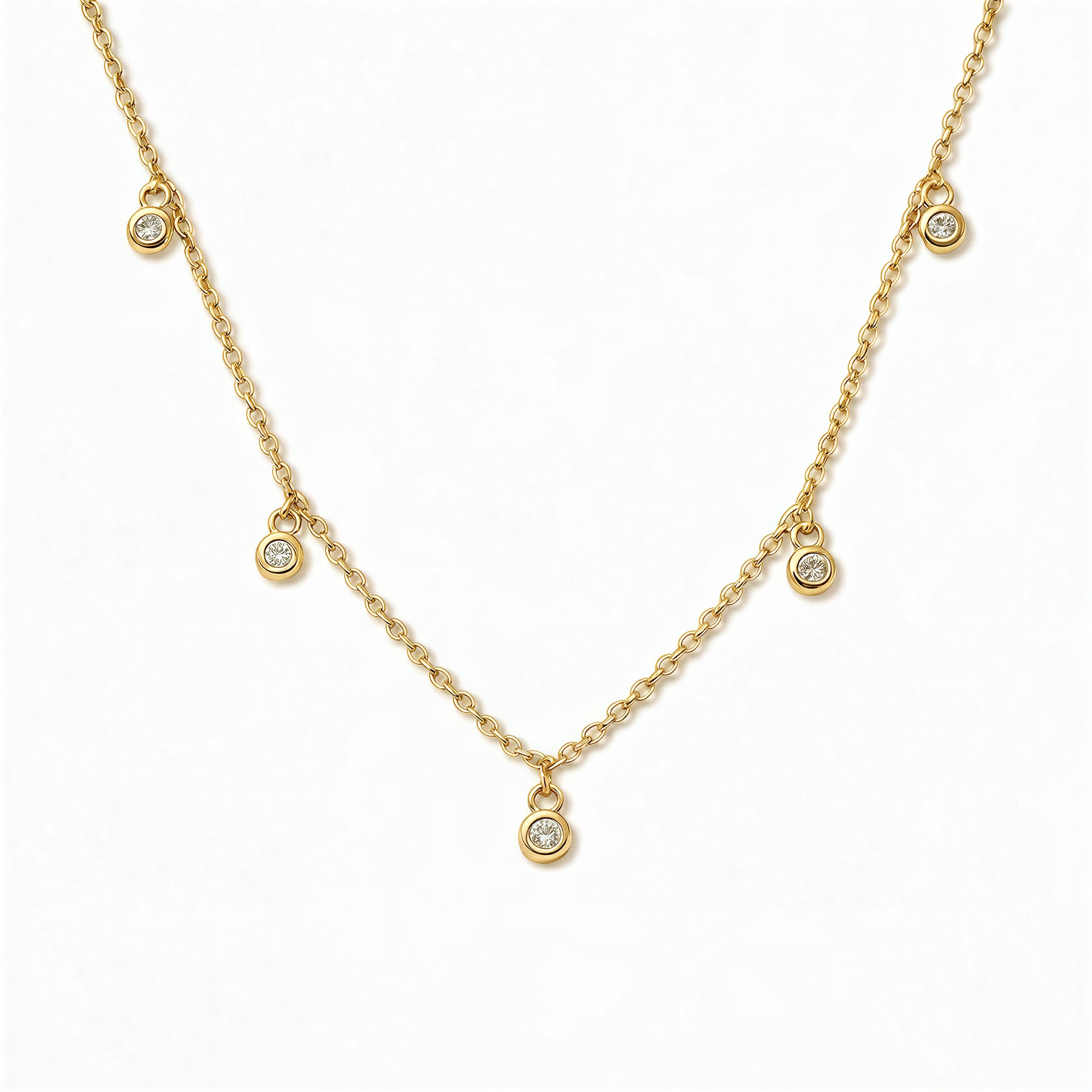 A Halo Bezel Set White Cubic Zirconia Drop Station Necklace by Skōsh Jewelry, featuring small bezel-set clear stones dangling at intervals along a fine gold chain, displayed against a white background.