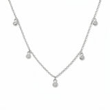 A Halo Bezel Set White Cubic Zirconia Drop Station Necklace by Skōsh Jewelry, featuring small bezel-set clear stones dangling at intervals along a fine sterling silver chain, displayed against a white background.