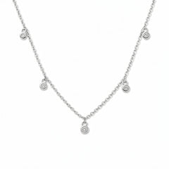 A Halo Bezel Set White Cubic Zirconia Drop Station Necklace by Skōsh Jewelry, featuring small bezel-set clear stones dangling at intervals along a fine sterling silver chain, displayed against a white background.