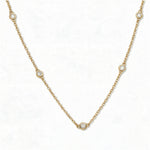 A Sanctuary Bezel Set White Cubic Zirconia Station Necklace by Skōsh Jewelry, featuring five small bezel-set clear stones spaced along a fine gold chain, displayed against a white background.