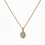 An Ethereal Opal with White Cubic Zirconia Halo Pendant Necklace by Skōsh Jewelry, featuring an oval iridescent opal framed by a halo of small clear stones on a fine gold chain, displayed against a white background.