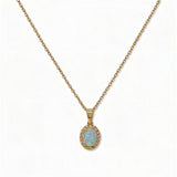An Ethereal Opal with White Cubic Zirconia Halo Pendant Necklace by Skōsh Jewelry, featuring an oval iridescent opal framed by a halo of small clear stones on a fine gold chain, displayed against a white background.