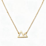 A Mountains and Valleys Necklace by Skōsh Jewelry, featuring an open outline of two mountain peaks set on a fine gold chain, displayed against a white background.