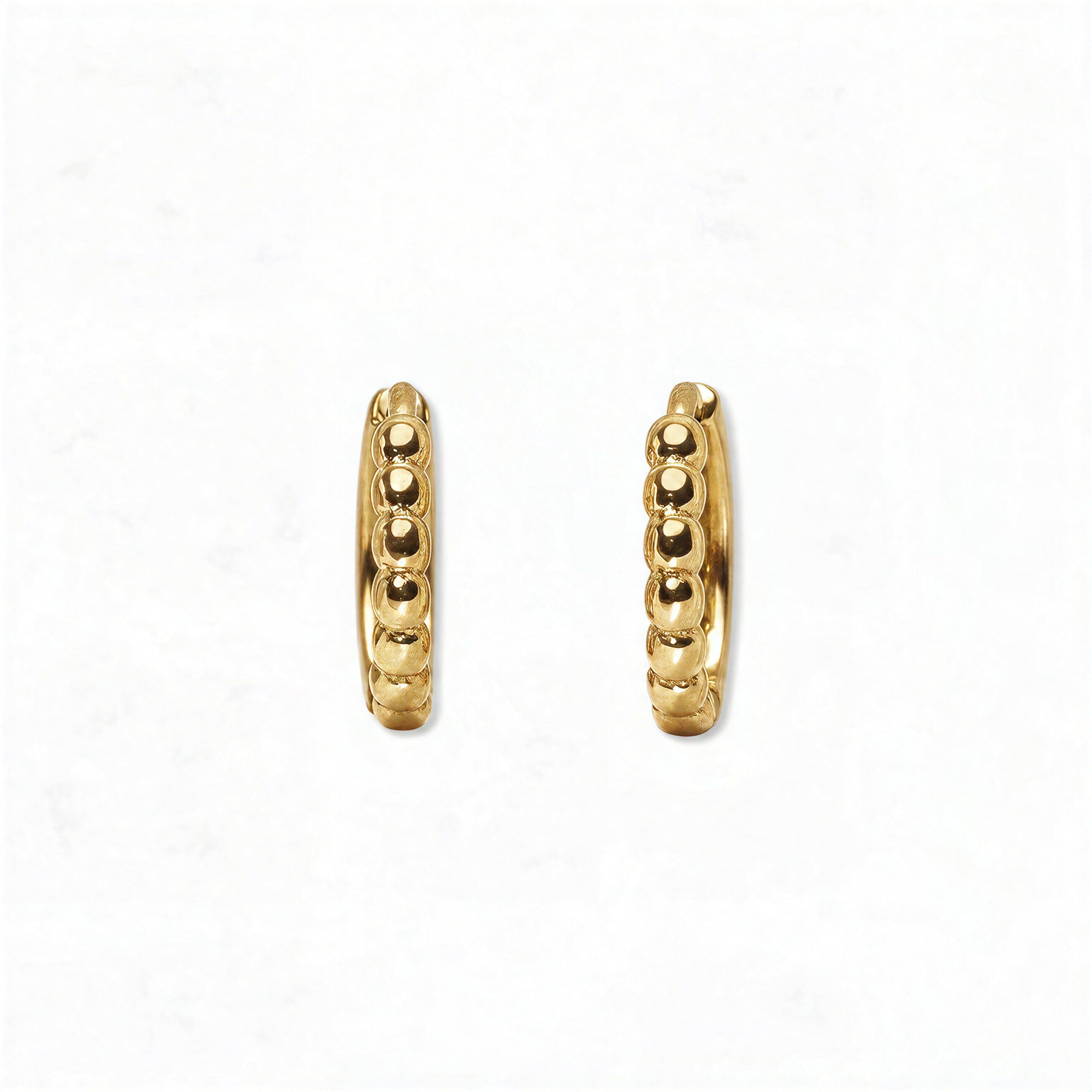 A pair of Beaded Huggie Hoop Earrings by Skōsh Jewelry, featuring small gold huggie hoops with a beaded texture, displayed against a white background.