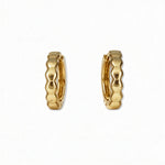 A pair of Hexagon Huggie Hoop Earrings by Skōsh Jewelry, featuring small gold huggie hoops with a faceted hexagon texture, displayed against a white background.