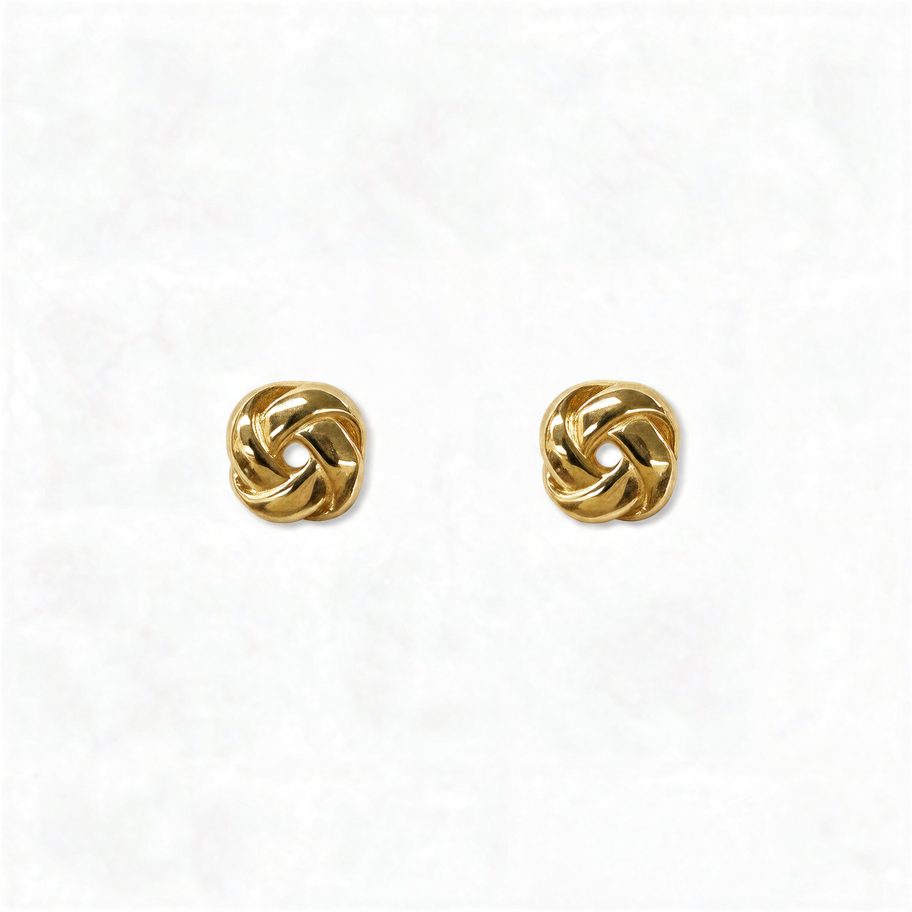 A pair of Knotted Stud Earrings by Skōsh Jewelry, featuring polished gold studs shaped like twisted love knots, displayed against a white background.