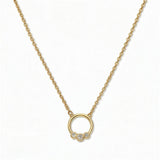 A Trio White Cubic Zirconia Accent Circle Necklace by Skōsh Jewelry, featuring a small open circle accented with three clear stones on a fine gold chain, displayed against a white background.