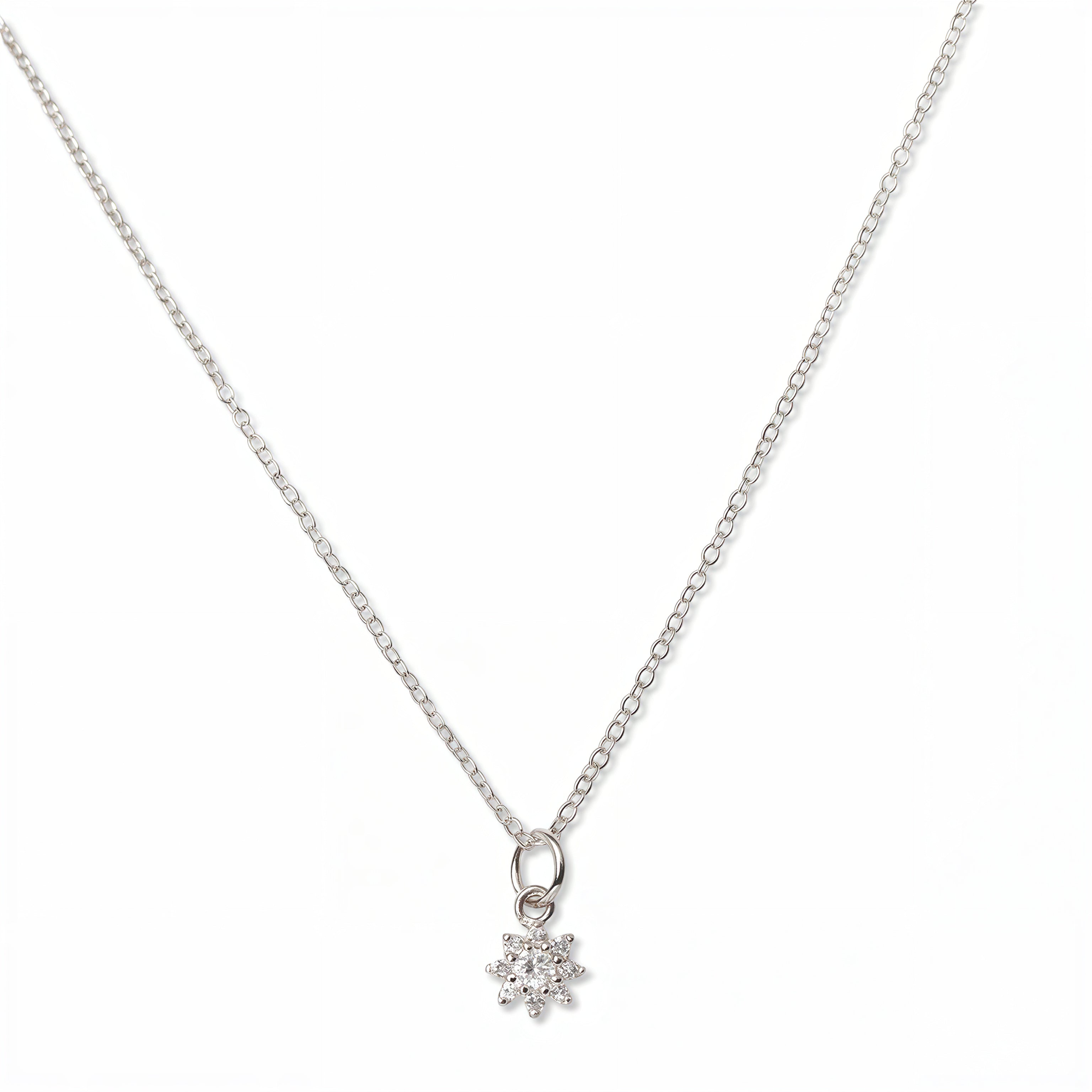 A Sunburst White Cubic Zirconia Pendant Necklace by Skōsh Jewelry, featuring a small sunburst pendant with a clear stone at its center on a fine sterling silver chain, displayed against a white background.