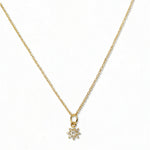 A Sunburst White Cubic Zirconia Pendant Necklace by Skōsh Jewelry, featuring a small sunburst pendant with a clear stone at its center on a fine gold chain, displayed against a white background.