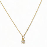 A Sunburst White Cubic Zirconia Pendant Necklace by Skōsh Jewelry, featuring a small sunburst pendant with a clear stone at its center on a fine gold chain, displayed against a white background.