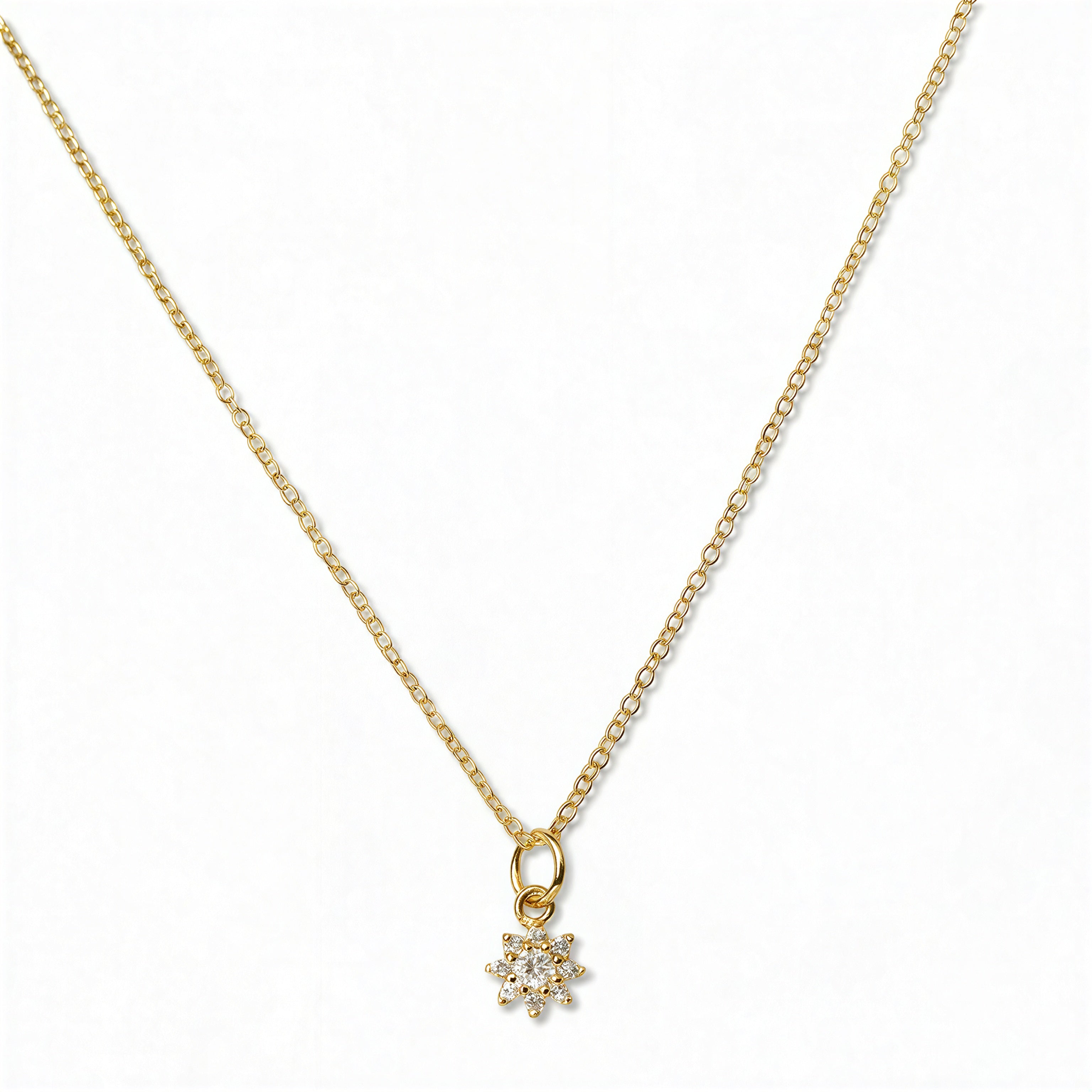 A Sunburst White Cubic Zirconia Pendant Necklace by Skōsh Jewelry, featuring a small sunburst pendant with a clear stone at its center on a fine gold chain, displayed against a white background.