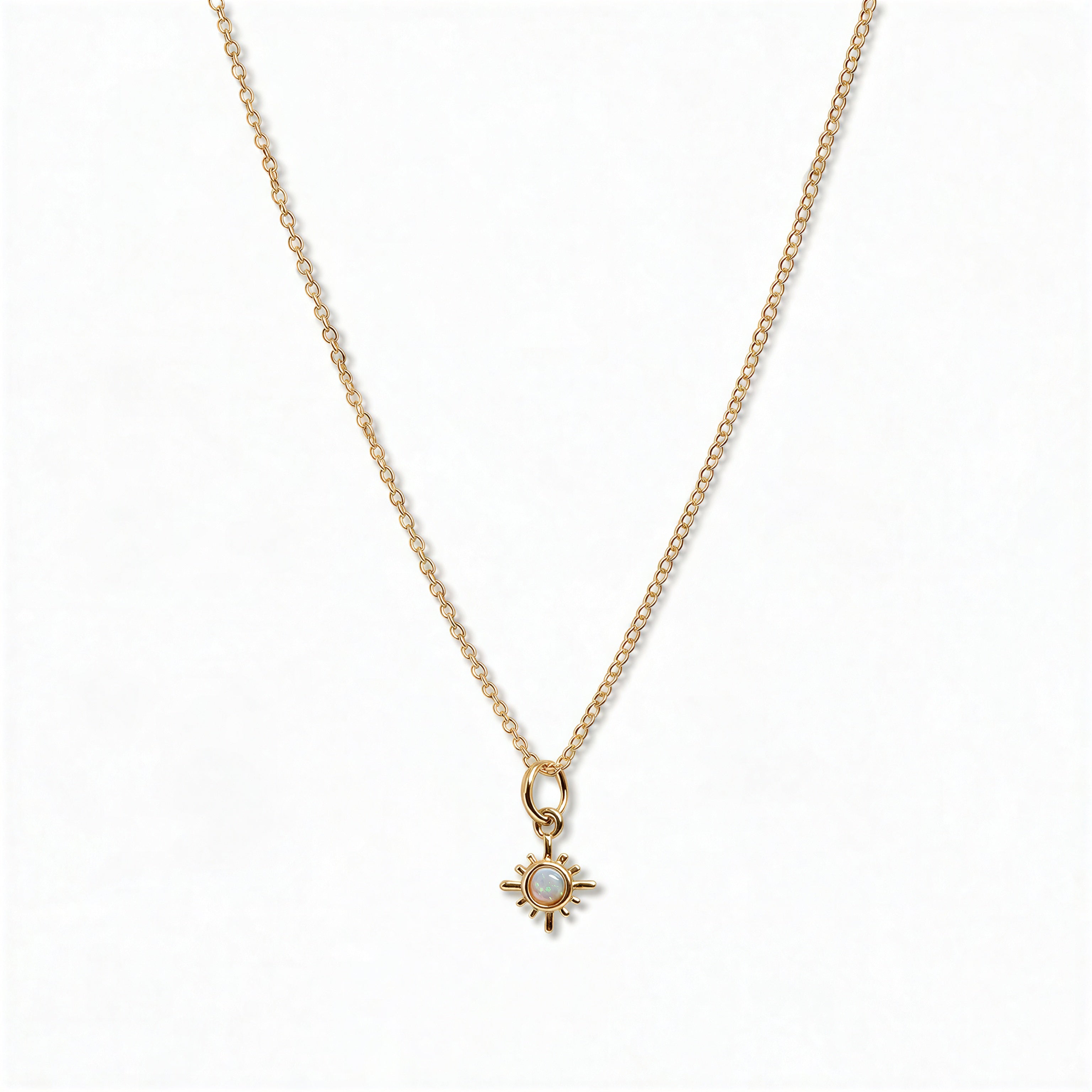 A Sunburst Opal Pendant Necklace by Skōsh Jewelry, featuring a tiny sunburst pendant with an opal center on a fine gold chain, displayed against a white background.