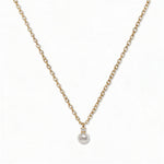 A Classic Drop Pearl with White Cubic Zirconia Accent Necklace by Skōsh Jewelry, featuring a round white freshwater pearl drop topped with a small clear stone on a fine gold chain, displayed against a white background.