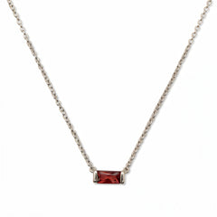 A January Birthstone Garnet Cubic Zirconia Baguette Necklace by Skōsh Jewelry, featuring a slim rectangular deep red baguette stone set horizontally on a fine sterling silver chain, displayed against a white background.