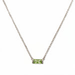 An August Birthstone Peridot Cubic Zirconia Baguette Necklace by Skōsh Jewelry, featuring a slim rectangular light green baguette stone set horizontally on a fine sterling silver chain, displayed against a white background.