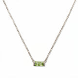 An August Birthstone Peridot Cubic Zirconia Baguette Necklace by Skōsh Jewelry, featuring a slim rectangular light green baguette stone set horizontally on a fine sterling silver chain, displayed against a white background.