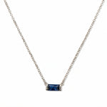 A September Birthstone Sapphire Cubic Zirconia Baguette Necklace by Skōsh Jewelry, featuring a slim rectangular deep blue baguette stone set horizontally on a fine sterling silver chain, displayed against a white background.