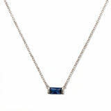 A September Birthstone Sapphire Cubic Zirconia Baguette Necklace by Skōsh Jewelry, featuring a slim rectangular deep blue baguette stone set horizontally on a fine sterling silver chain, displayed against a white background.