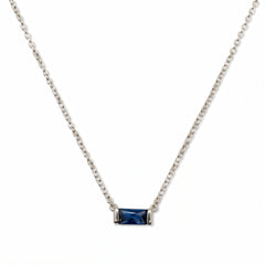A September Birthstone Sapphire Cubic Zirconia Baguette Necklace by Skōsh Jewelry, featuring a slim rectangular deep blue baguette stone set horizontally on a fine sterling silver chain, displayed against a white background.